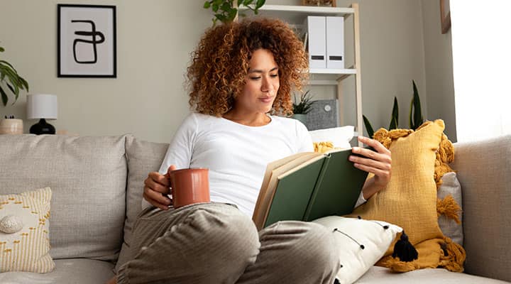 Woman drinking tea on the couch while reading a book