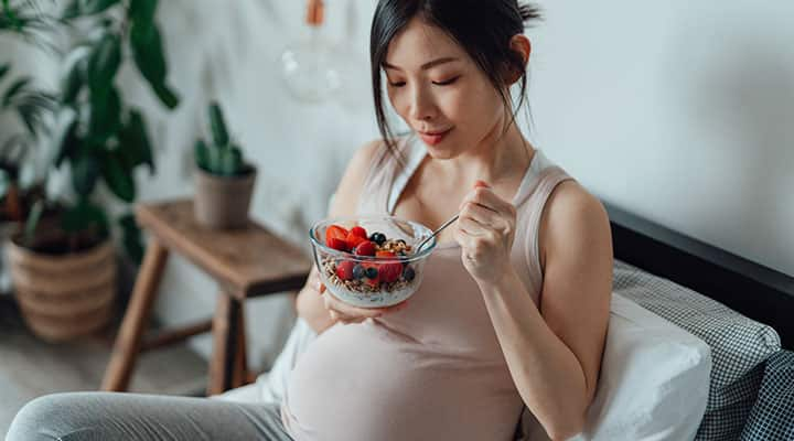 Pregnant woman eating yogurt with probiotics to help with morning sickness