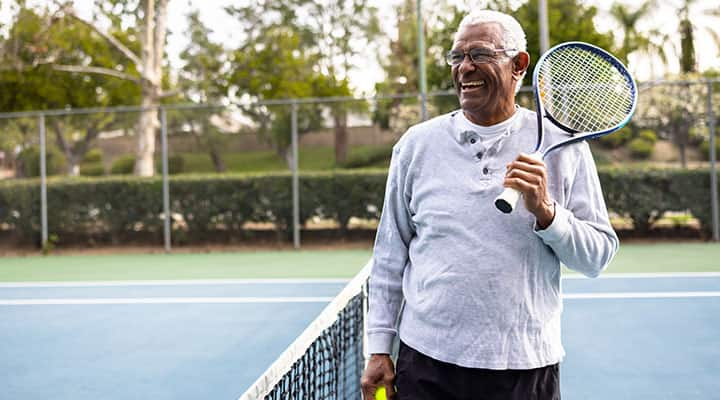 Older man playing tennis outside to keep his muscles and bones healthy