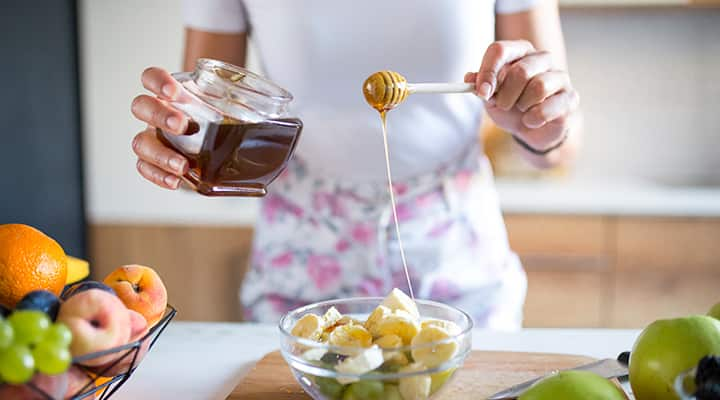 Woman drizzling local honey onto fruit to sweeten and prevent allergies.