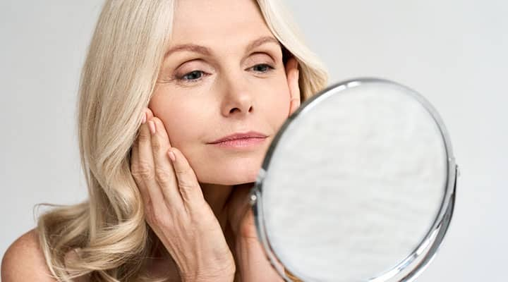 Older woman looking in the mirror to examine the effects of a retinyl palmitate