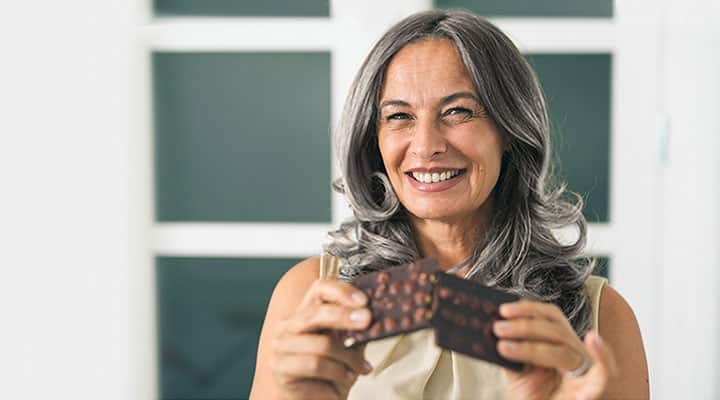 Smiling middle-aged woman breaking a nut-filled chocolate bar