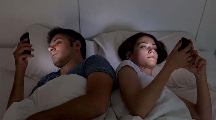 Man and woman laying in bed looking at cell phones