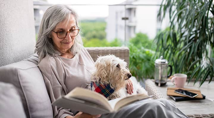 Healthy elderly woman on couch reading a book with her dog