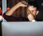 man in front of computer, lifting glasses to rub strained eyes