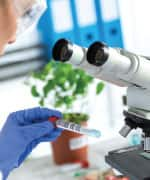 Scientist reading sample tube next to a microscope