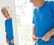 Man measuring his waist and smiling in the  mirror