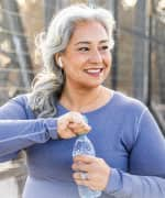 Woman smiling, opening a water bottle after exercising