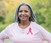 Smiling woman with breast cancer pink ribbon on shirt with intake of multivitamins