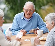 Senior friends laughing while playing cards that are at risk of brain diseases