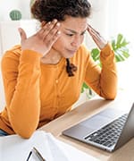 Woman rubbing temples and staring at laptop finding trouble focusing through brain fog