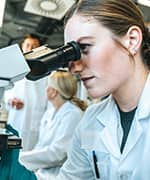 Lab researcher looking through microscope to study mango leaf extract for mental symptoms