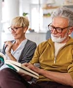 Senior couple sitting on couch reading books to combat cognitive disorders