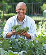 Older smiling man holding up broccoli head that is favorable for risk factors