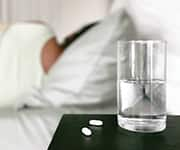 Glass of water with pills being used to alleviate sleep disorders