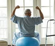 Older man sitting on yoga-ball for physical therapy